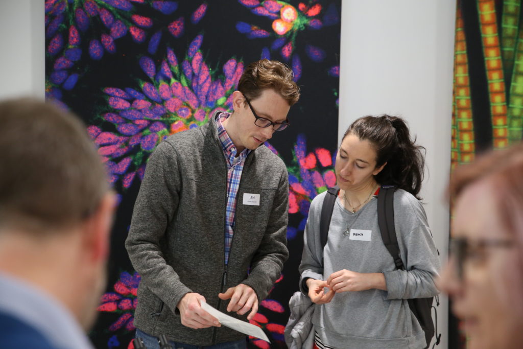 Two people engaging in conversation in front of a large piece of brightly coloured scientific artwork