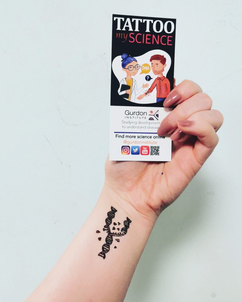 Hand with a DNA replication tattoo on the wrist holding the Tattoo my Science card
