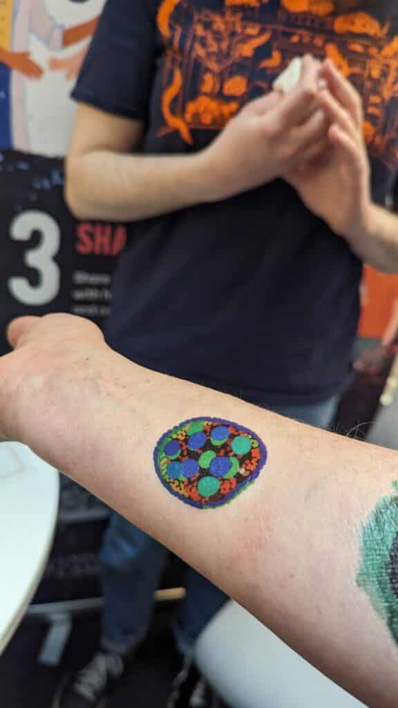 An outstretched forearm with a colourful "Fruit Fly Egg Chamber" tattoo