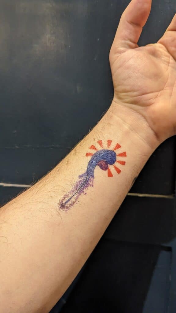 An outstretched arm with the "Under Pressure" tattoo showing a blue chick embryo and red markings to show pressure on the embryo