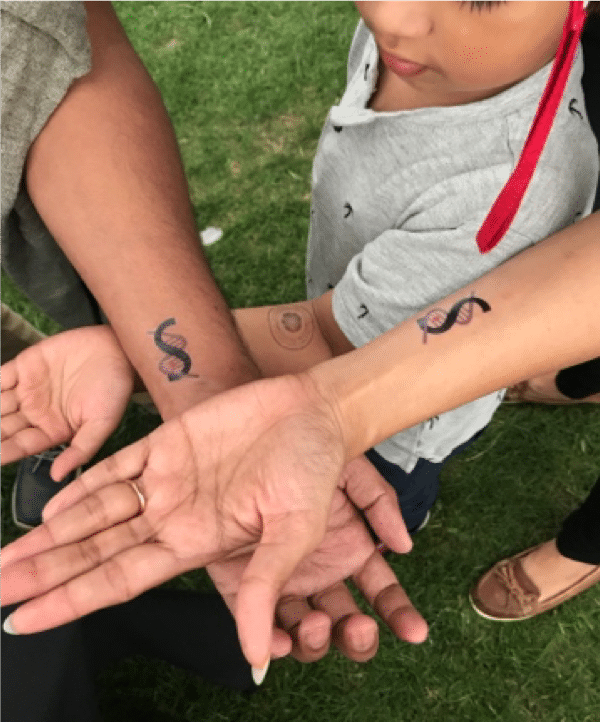 Three hands crossed over, each with a scientific tattoo on the wrist