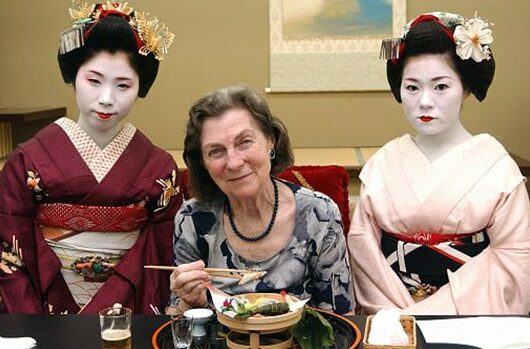 Anne McLaren seated between two Japanese geishas, eating from a bowl