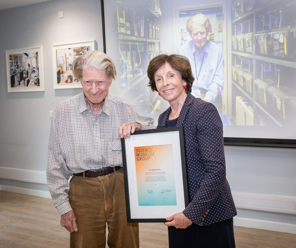 Sir John Gurdon and Dame Mary Archer pose with the framed SMG Fellowship award
