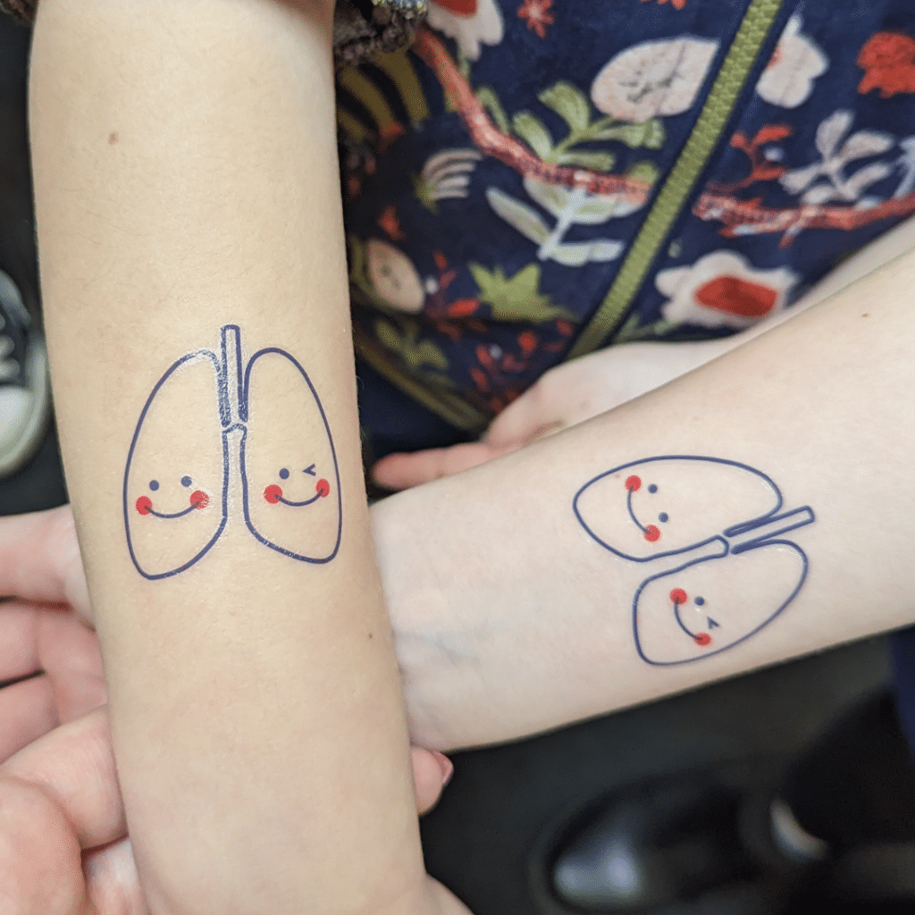 Two children's forearms with tattoos of lungs with smiley faces